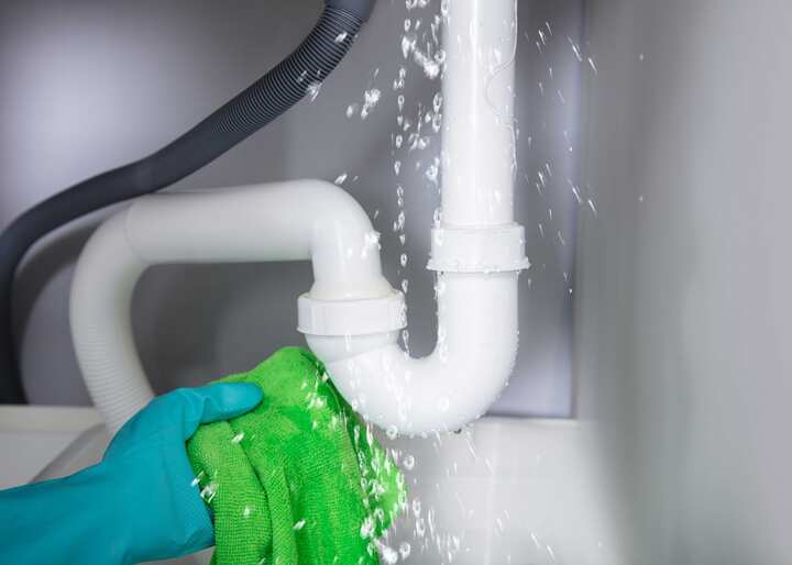 A gloved hand holding a rag trying to capture the water leaking from a pipe in Bowling Green, KY